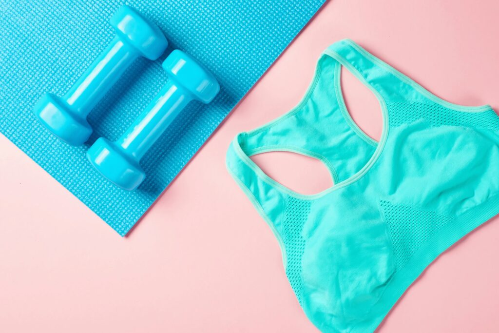 Fitnes minimalism concept. Dumbbells and sport bra on a blue and pink backgroundm top view